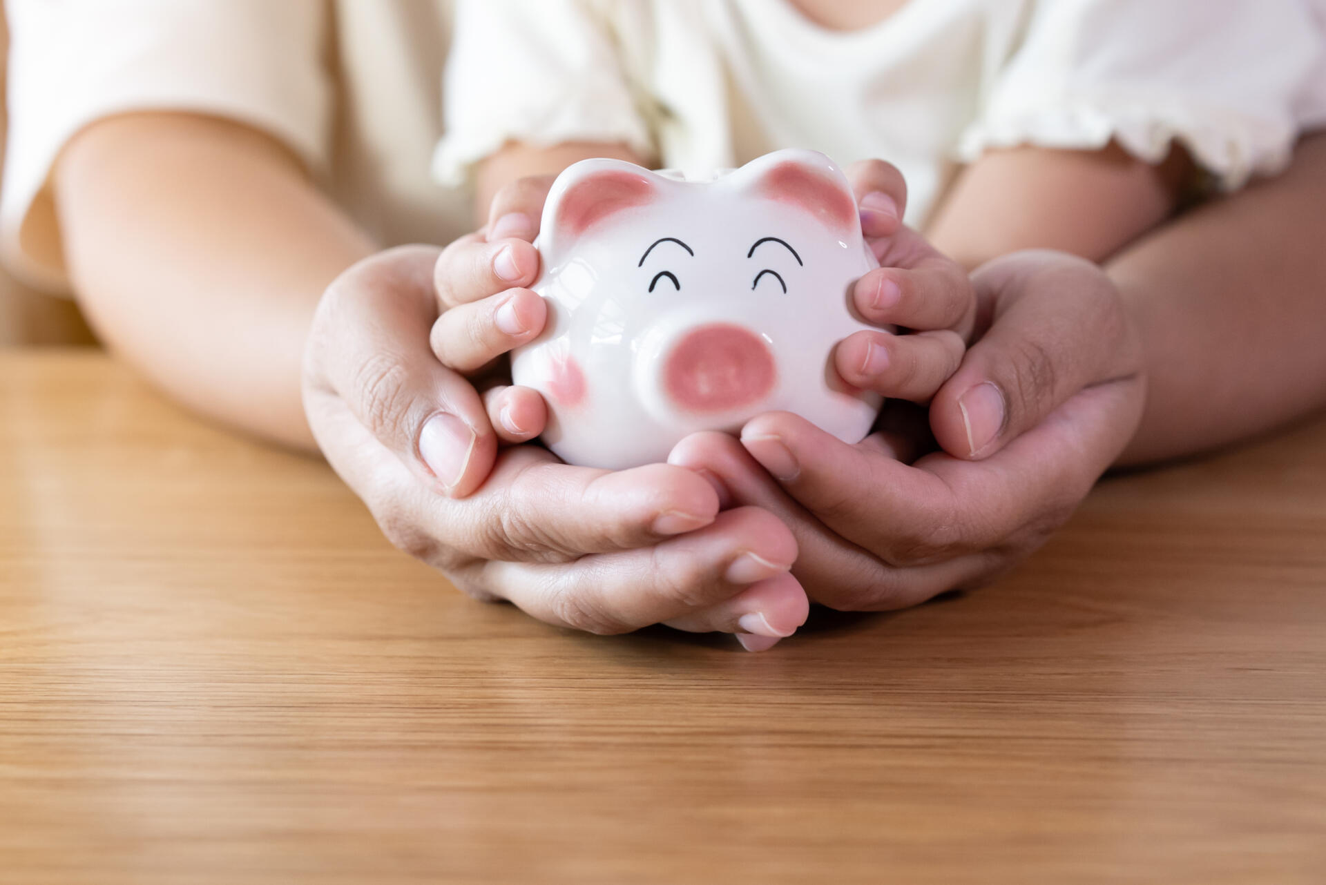 Sparschwein in Händen von einem Kind und einem Erwachsenen