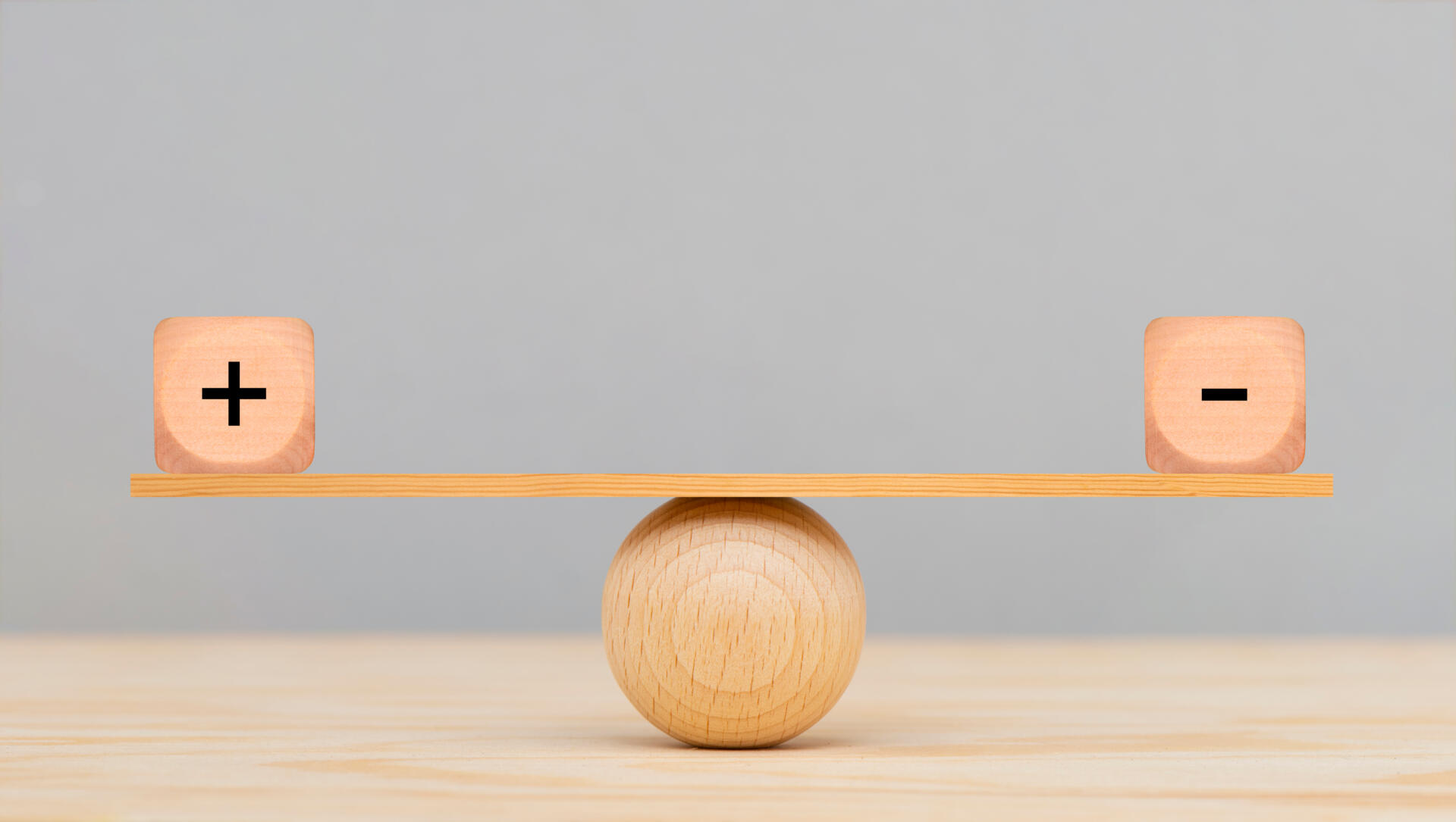 Holzwaage mit Würfel mit jeweils Plus und Minus darauf